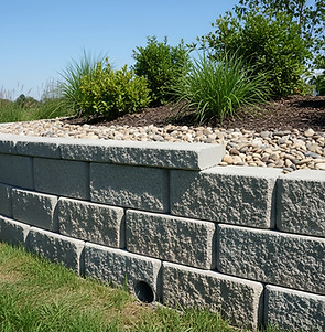 A beautiful retaining wall curves around a garden bed filled with plants and decorative ro