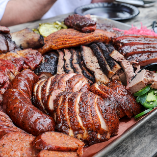 Close-up of a barbecue platter with smoked meats, sausage, and jalapeños being served at Bar-A-BBQ in Montgomery, Texas.