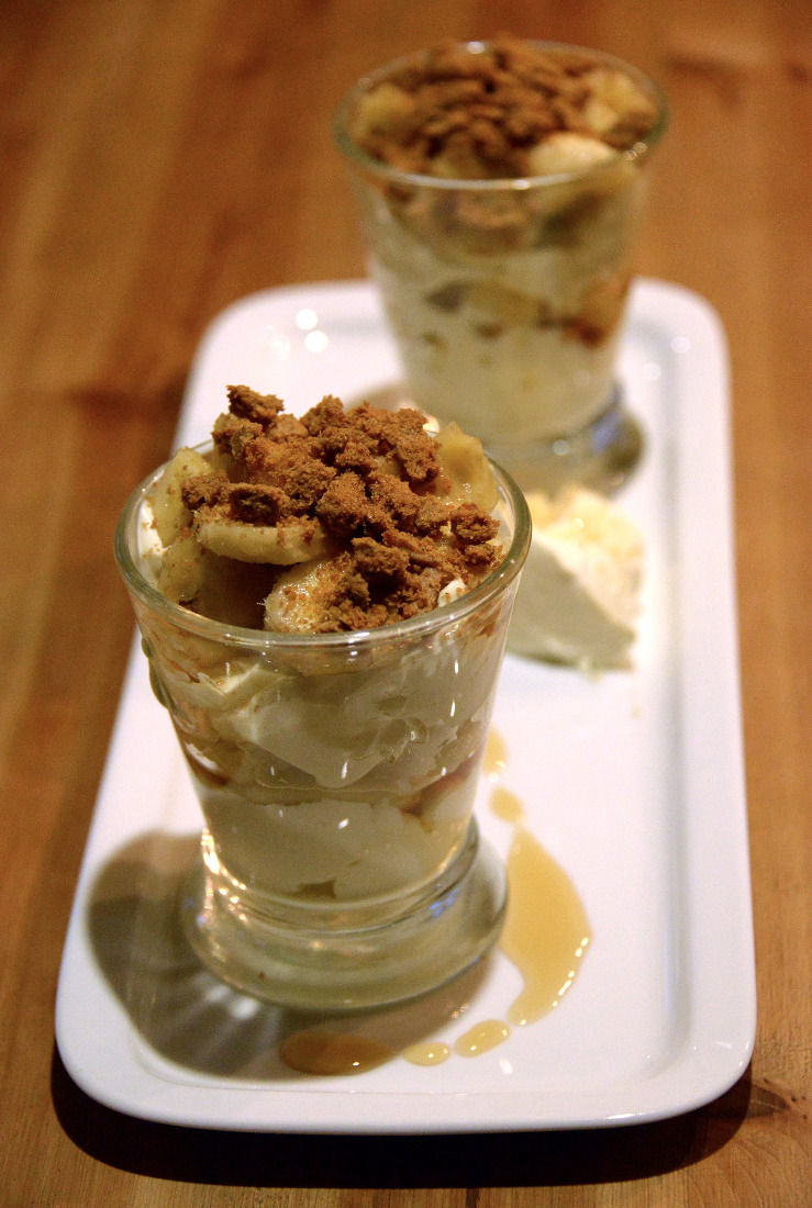 Dans des verres, alternance de rondelles de banane et de fromage blanc à la crème et au chocolat blanc ; miettes de speculoos sur le dessus.