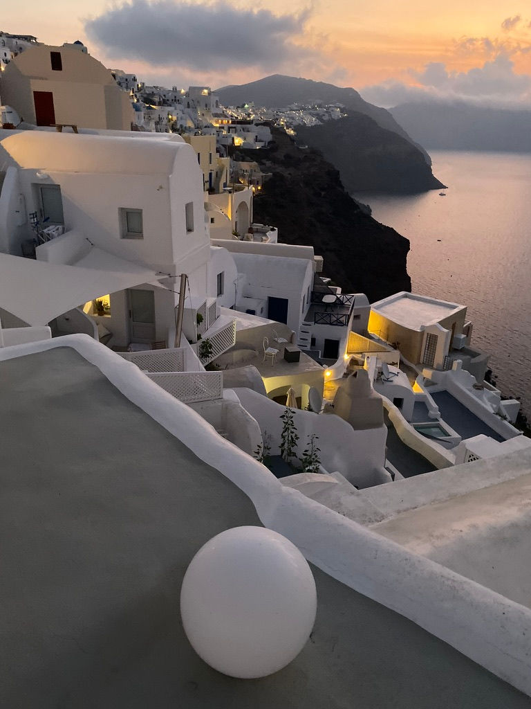 As twilight falls over Oia, the village glows with quiet grace—each curve and terrace catching the last breath of light from a mythic sky.