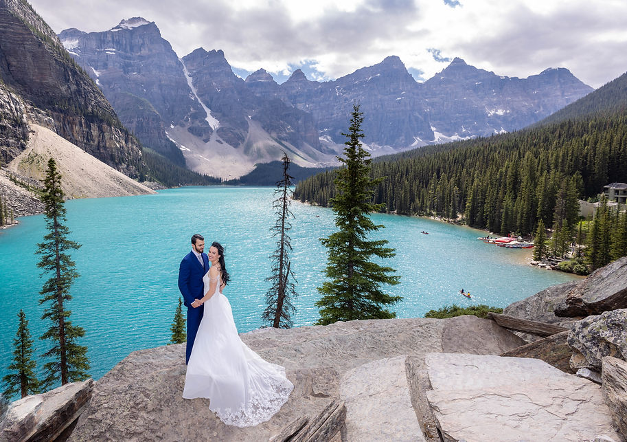 Wedding couple in front of Moraine lake and the stunning turquoise water on rock pile with jagged peak backdrop