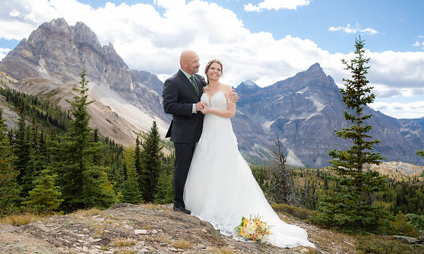 Wedding couple with white dress and suit in front of mountain backdrop in Banff National park
