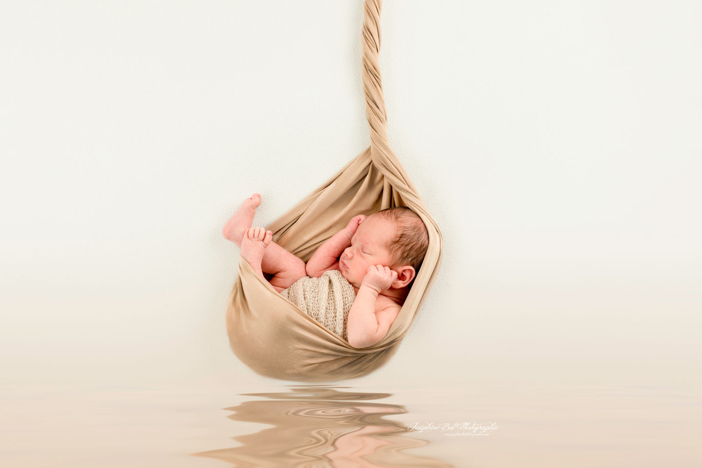 Nouveau-né dormant paisiblement dans un hamac beige avec ses pieds levés. Fine art Joséphine Bot photographe