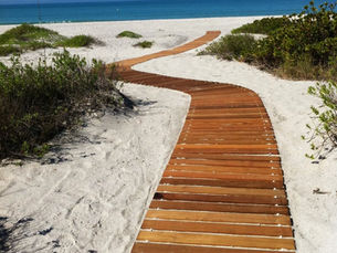 Curved Mister Boardwalk® Roll-Out Boardwalk winding through white sand dunes to the beach, providing durable waterfront access with minimal impact on the surrounding landscape.