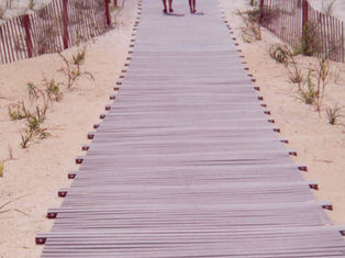 A 48-inch-wide Mister Boardwalk® Roll-Out Boardwalk with no spacing and outboard connectors extends across sandy beach dunes toward the shoreline. A woman and child walk side by side on the wide boardwalk, bordered by dune fencing and native beach vegetation.