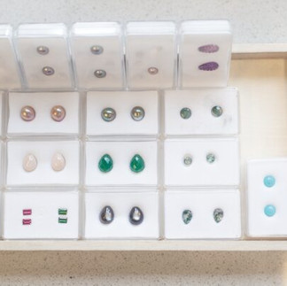 Ulike edelstener i hvite beholdere og en trekasse, mange farger og former.