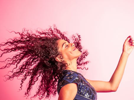 Pink background with woman with smile on face dancing with curly hair flying free
