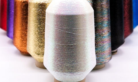 Cones of various coloured lurex yarns on a white background