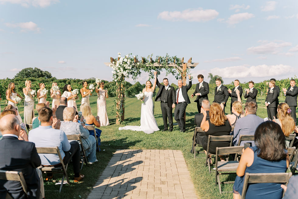 Bride and groom holding hands cheering as they just officially got married and people are celebrating with them on a sunny day. 