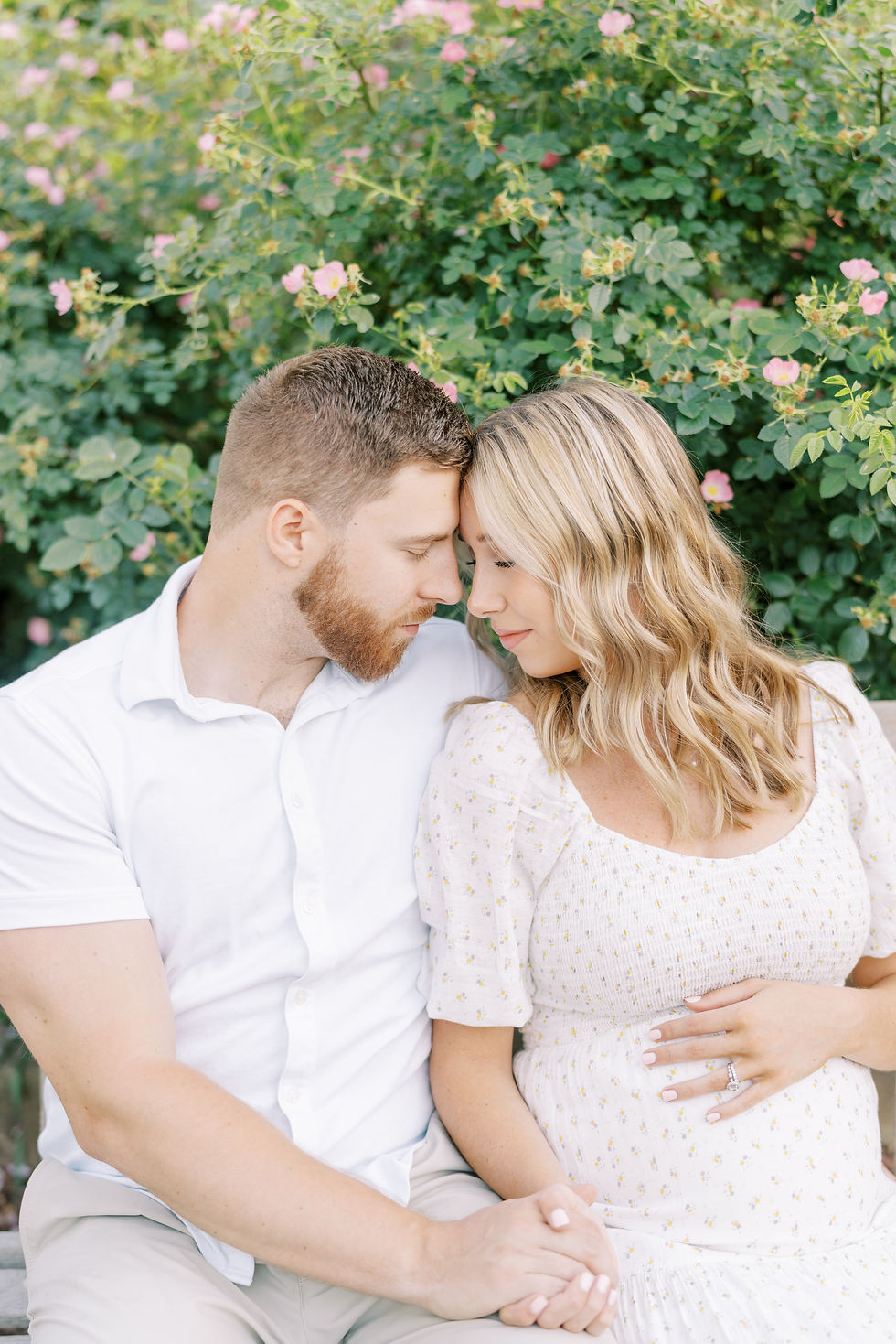 man and woman have foreheads together holding hands and a hand on baby bump