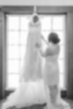 backlit wedding dress hanging on window with bride in white robe