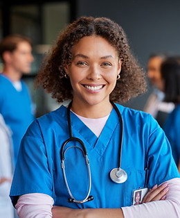 Confident happSimplicit HealthSimplicit Health Aty woman nurse smiling with crossed arms with healthcare team in background.