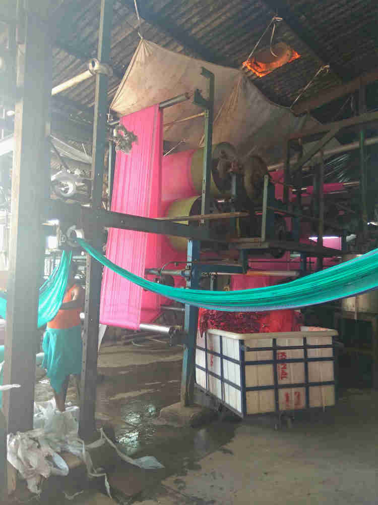 עובד במכנסים קצרים וכפכפים לצד חומרים מסוכנים במפעל טקסטיל בהודו