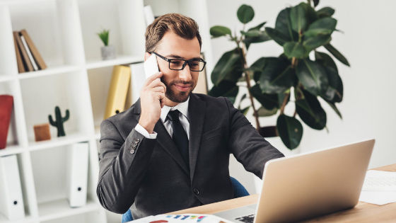 man in suit using his phone infront of a laptop researching about thought leadership