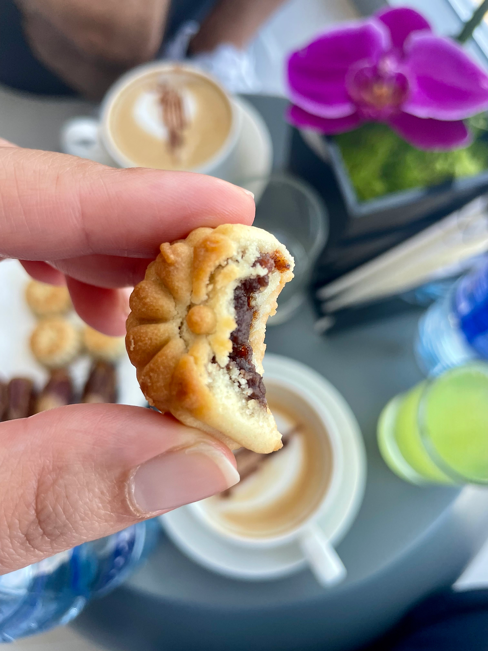 Hand holds a bitten date filled cookie over coffee cups, with a purple orchid with Middle Eastern Dishes in the background at the Burj Khalifa Tower in Dubai.