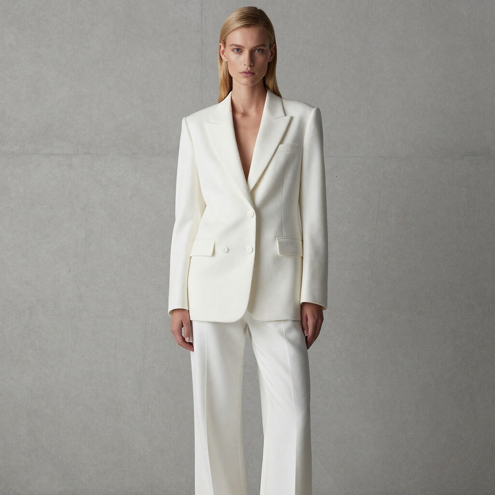 Studio photography of a woman posing in stylish casual wear. She stands confidently against a seamless beige backdrop in a well-lit space.