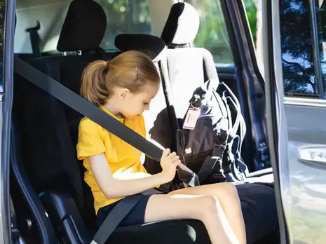 A child putting on her seatbelt in the back of a vehicle.