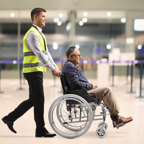 Airport attendant pushing a passenger in a wheelchair through the terminal for accessible transportation assistance.
