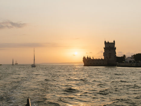 Vue du coucher de soleil à Lisbonne depuis un bateau sur le Tage, avec la ville illuminée à l’arrière-plan.