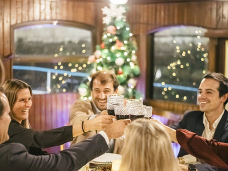 Grupo a brindar num jantar de Natal em Lisboa a bordo da Royal Marine, com luzes e decoração festiva sobre o Tejo.
