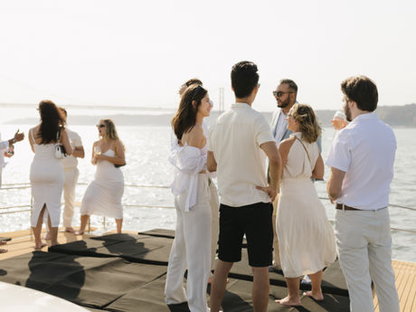 Grupo de personas elegantes a bordo de un catamarán en Lisboa, durante un evento corporativo al atardecer, con vistas al Puente 25 de Abril.