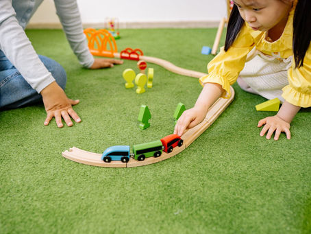 Preschool girl playing with a wooden toy train on the floor