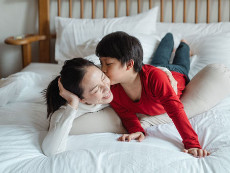 Young son hugging and kissing his mother on the bed, feeling calm and safe