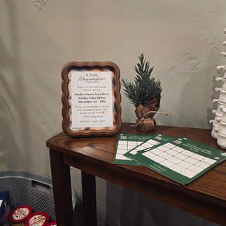 Small decorative evergreen tree (totally fake), on a small wood table with green chamber bingo cards next to it and a wood framed print of the Suite November collaboration