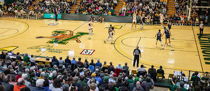 An overview of a University of Vermont basketball game with players on the court and fans in the stands.