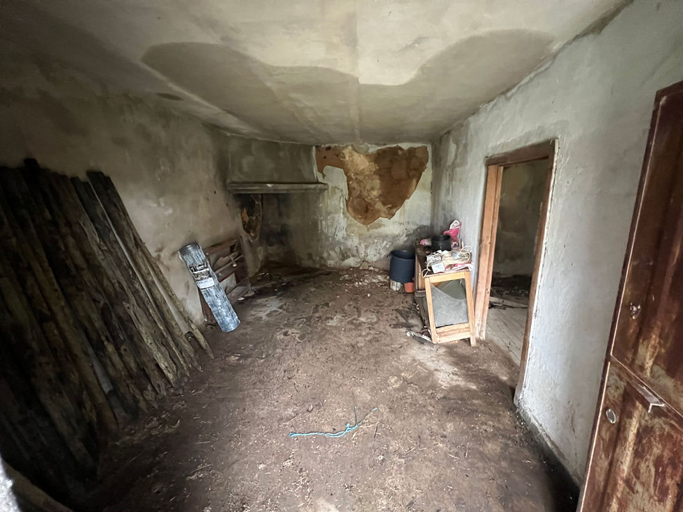 Interior of an old building showing damp marks, crumbling plaster, and clutter on the floor.