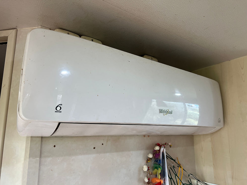 Wall-mounted indoor air conditioner unit (Whirlpool) near the ceiling, with light stains above and a small shelf below.