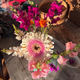 Overhead view of a floral bouquet featuring a central Gerbera daisy and snapdragons, with a person seated in the background.