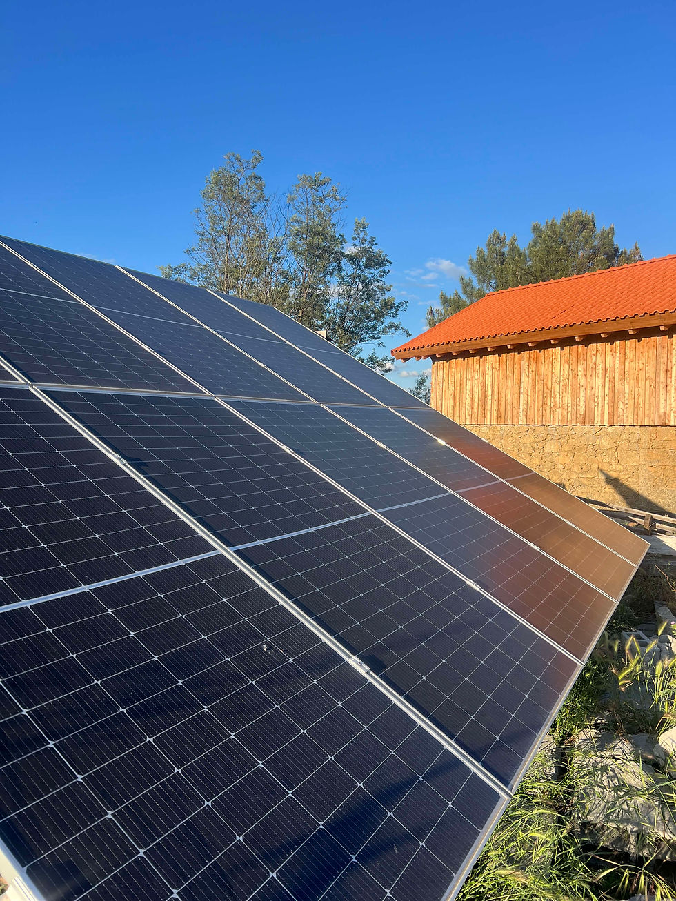 Ground-mounted solar panels angled toward the sun beside a wooden building with a red tiled roof.