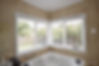 A bathroom with large windows fitted with white wooden venetian blinds