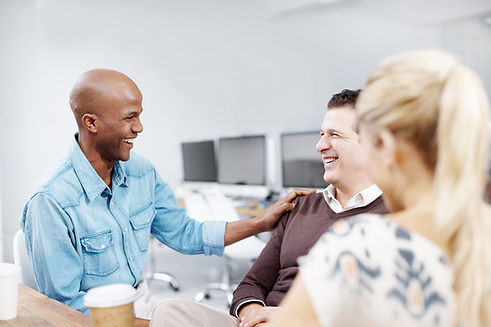 Two men smiling at a table, one offering a supportive gesture