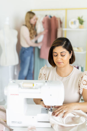 Woman sewing on machine, colleague viewing clothes