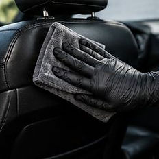 Gloved hand wiping leather car seat for odor elimination