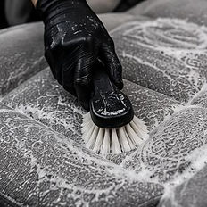 Person scrubbing a car seat with soap and a brush.