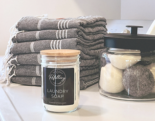 Refillable laundry soap jar, stacked towels, and wool dryer balls — home goods available at One Drop Refillery