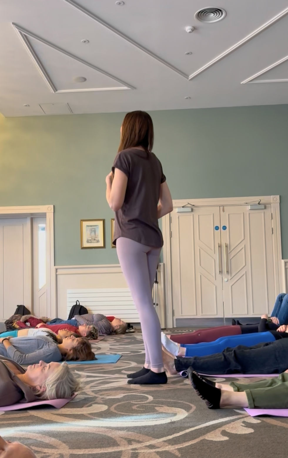 Team wellbeing session hosted by Lisa, leading a group breathwork or relaxation exercise, with participants lying on yoga mats in a calm, light-filled venue.