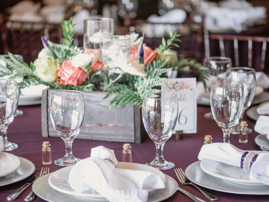 A close up of the table top decor for a wedding with plates, flatware, napkins, glasses, and floral centerpiece