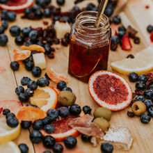 A picture showing a charcuterie board with fresh and dried fruits and  honey