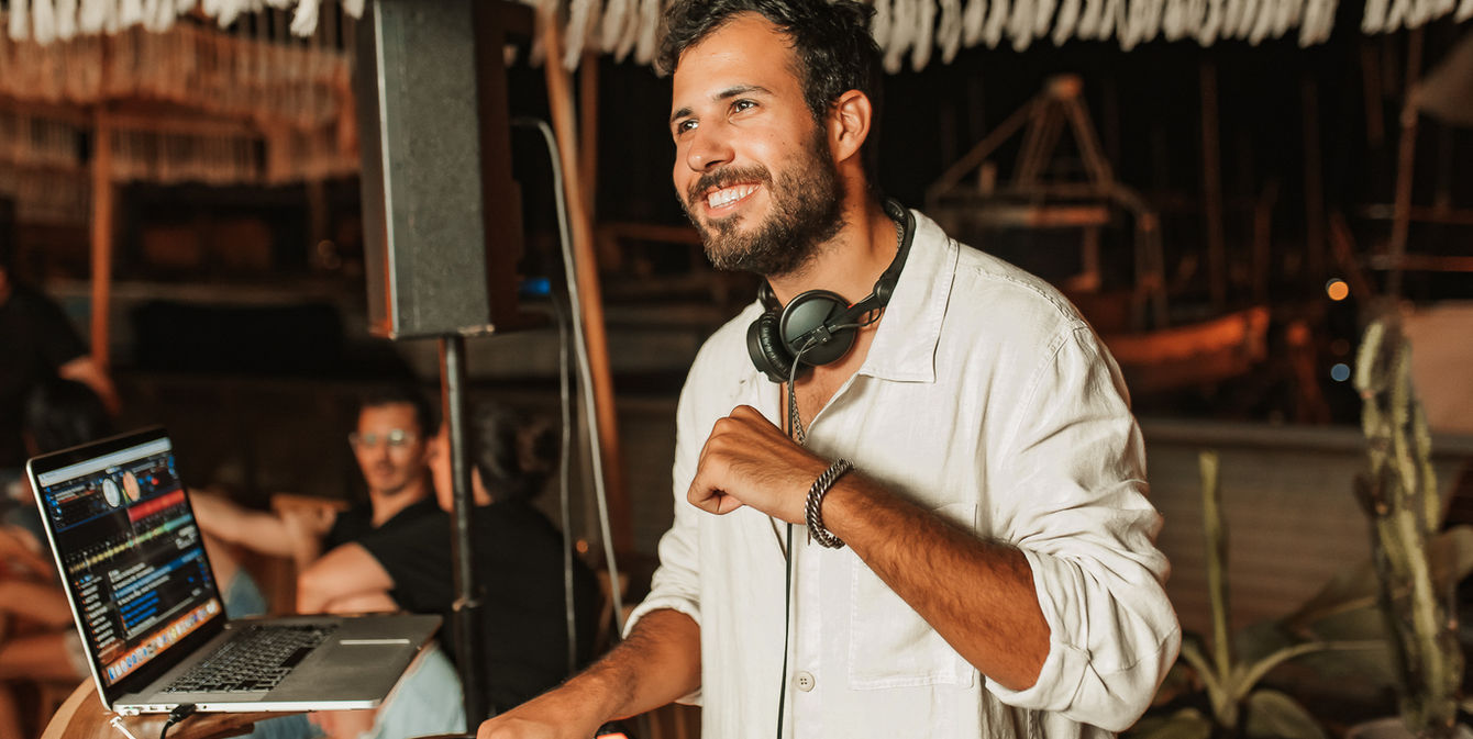 Smiling DJ playing music at night event with laptop and headphones Stolero Events