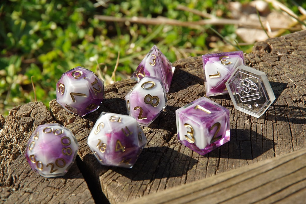 Set de dés violets et blancs artisanal La Looterie posé sur une souche en bois, chiffres dorés, photo en extérieur
