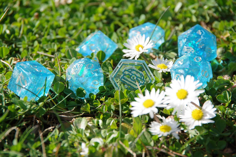 Dés de JDR bleu turquoise La Looterie brillants au soleil, disposés dans l’herbe parmi des pâquerettes