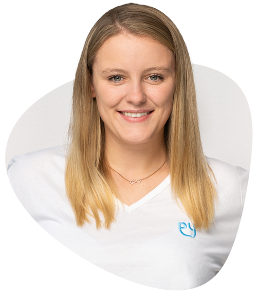 Lächelnde Pflegefachkraft mit blondem Haar, weißem Shirt mit Logo, weißem Hintergrund, vor dem Einsatz der Grundpflege.