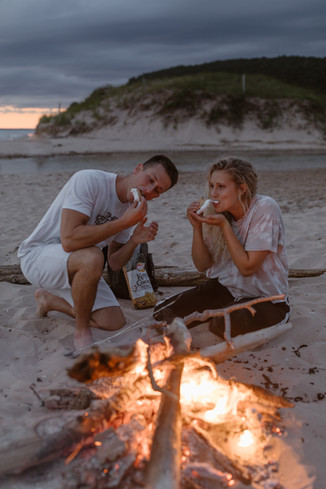 couple eating s'mores by a fire pit on the beach on their elopement day