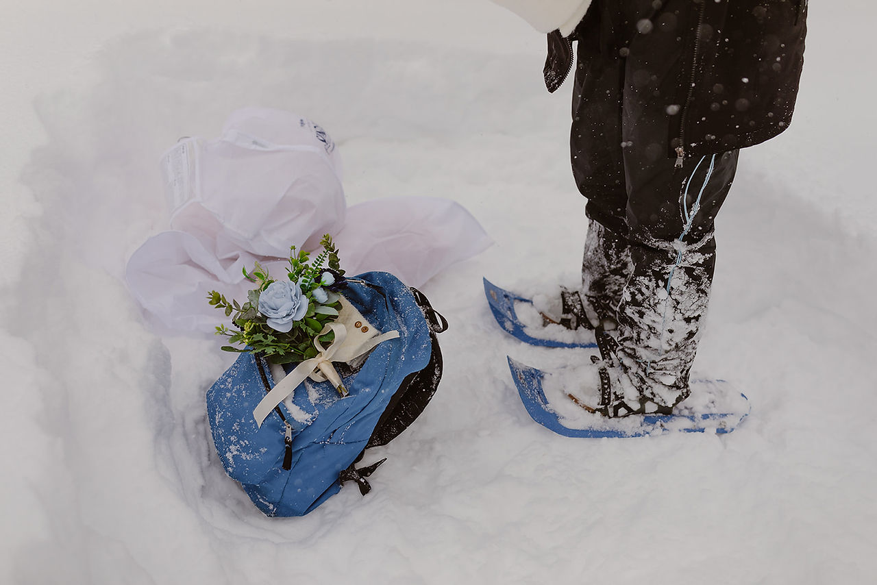 Bride in snowshoes getting dressed in the snow on her winter elopement day