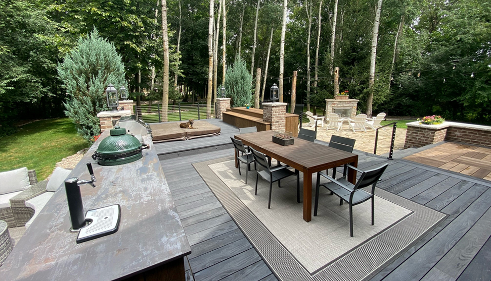 Large deck with smoked ask millboard decking, patio furniture and rug on the deck with large green trees in the background