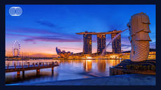 Singapore skyline at sunset with Marina Bay Sands, Merlion statue, and the Singapore Flyer. Vibrant sky and reflections on water.